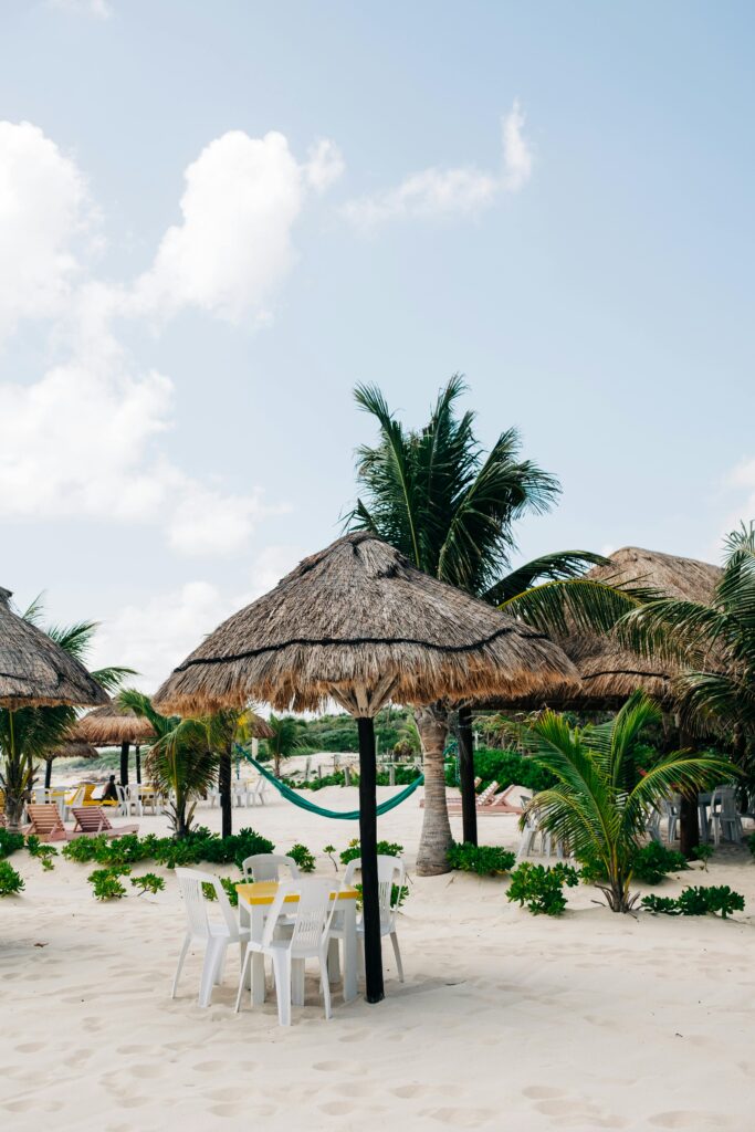 Relaxing beach setup with palapa umbrellas and palm trees in Cozumel, Mexico.