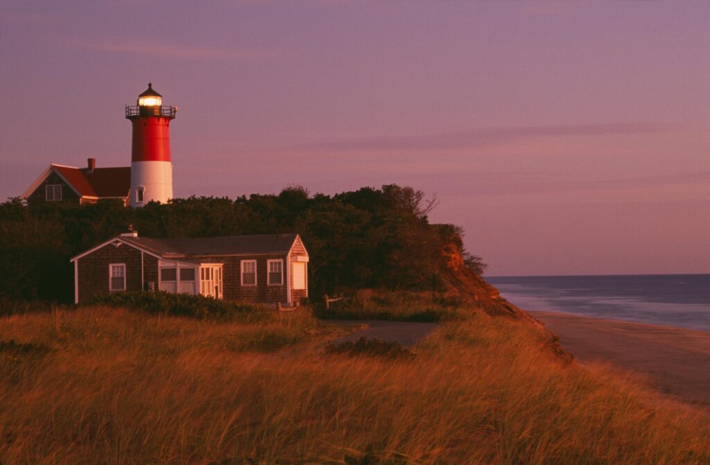 Dramatic view of Nauset Lighthouse in Massachusetts surrounded by coastal landscape at sunset.