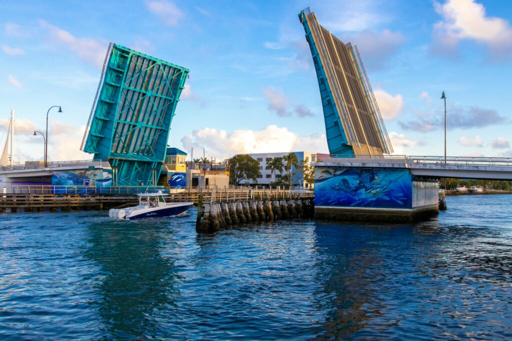 A boat sails through a vibrant blue drawbridge on a sunny day, capturing urban waterfront life.