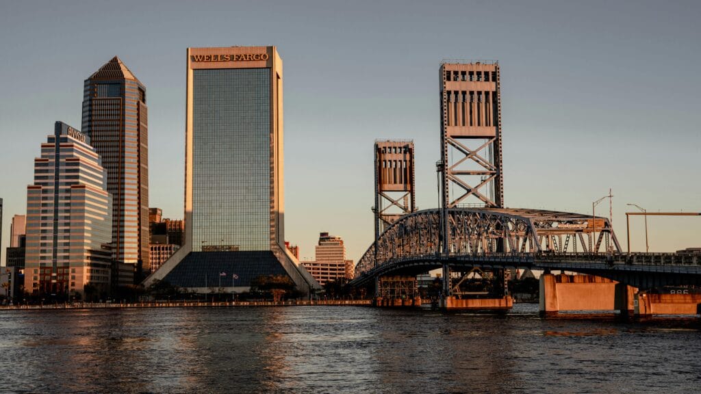 Stunning view of Jacksonville, FL skyline at sunset with iconic bridges and modern skyscrapers reflecting on the water.