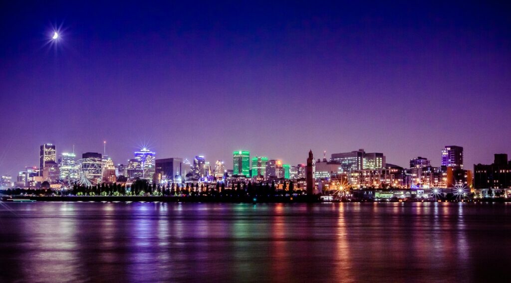 A stunning nighttime view of Montreal's skyline reflecting on the St. Lawrence River under a crescent moon.