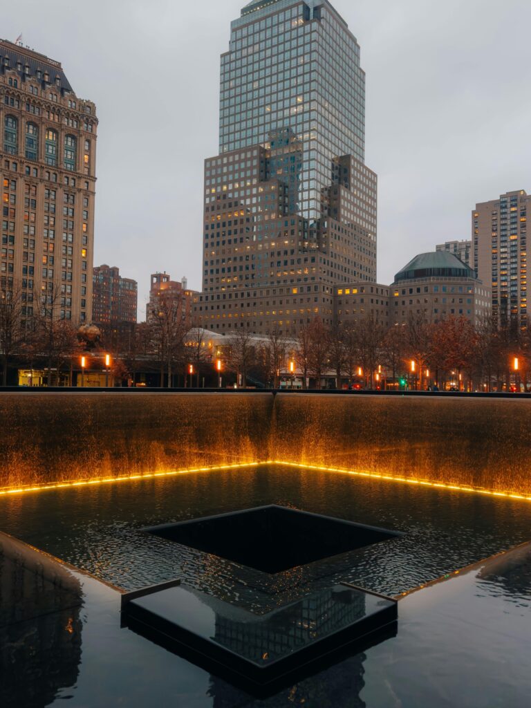 9/11 Memorial reflecting pool with city skyline at dusk in New York City.
